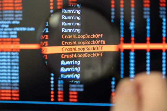 Man's hand holds magnifying glass over screen displaying highlighted CrashLoopBackOff error messages, symbolizing critical debugging work