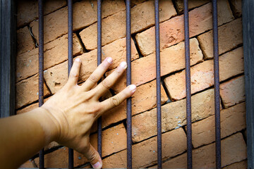 Hand Touching a Brick Wall Behind Metal Bars in Close-Up View