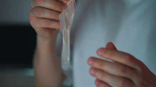 used condom in a man's hands.
A man holds an unsealed condom in his hands in a room.
Protection during sex.
Close-up of a latex condom