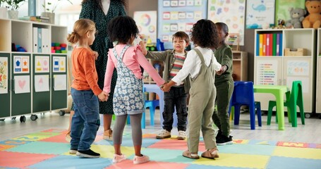 Group, children and holding hands with teacher in circle for playing, game and fun activity at...