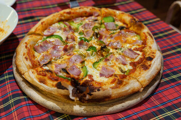 Homemade baked pizza topped with ham, green bell pepper and melted cheese on tartan tablecloth