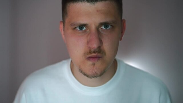A man clenches his cheekbones and lips in anger close-up.
Angry guy looking at the camera.
Angry and aggressive look of a guy in a dark room.
A man in a bad mood
