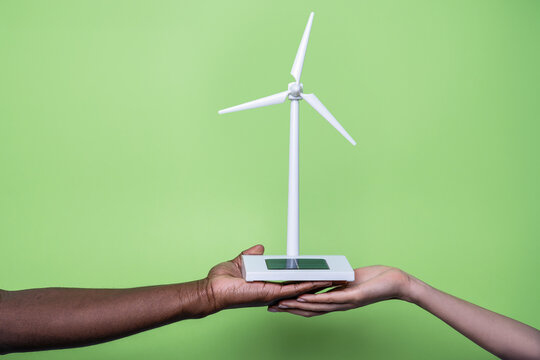 Multiethnic hands holding wind turbine model on green backdrop