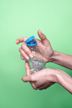Hands crushing plastic bottle against green background