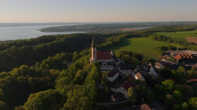 Luftaufnahme Kloster Andechs bei Muuenchen, Bayern. Drohnenvideo Wallfahrtskirche auf dem Heiligen Berg am Ammersee mit Landschaft, See und Sonnenuntergang. Burg Andechs. Braustuberl des Klosters. 