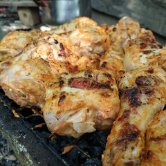 Raw marinated chicken drumsticks on outdoor grill. Spicy raw chicken drumsticks are arranged on a grill over charcoal outdoors, ready to be cooked for a barbecue meal.
