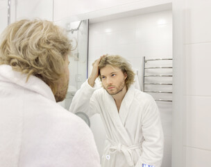 Obraz premium morning routine, young man looking in mirror in bathroom