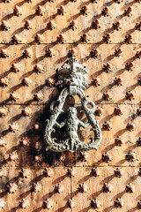 Ornate bronze door knocker with mythological figure on studded medieval wooden door in the historic center of Genoa