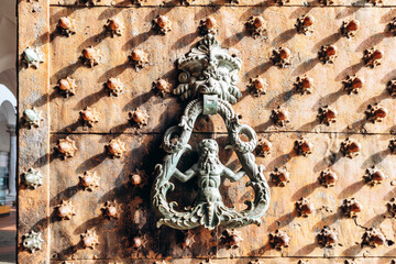 Ornate bronze door knocker with mythological figure on studded medieval wooden door in the historic center of Genoa