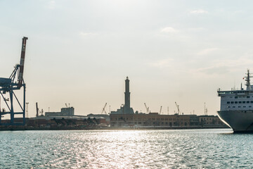 Genoa, Italy - September 22, 2024: Silhouette of Lanterna lighthouse, container cranes, and cruise ship in the busy port at sunset.