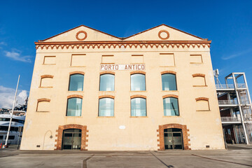 Genoa, Italy - September 22, 2024: Porto Antico waterfront with boats, modern attractions, and historic buildings under a clear sky.