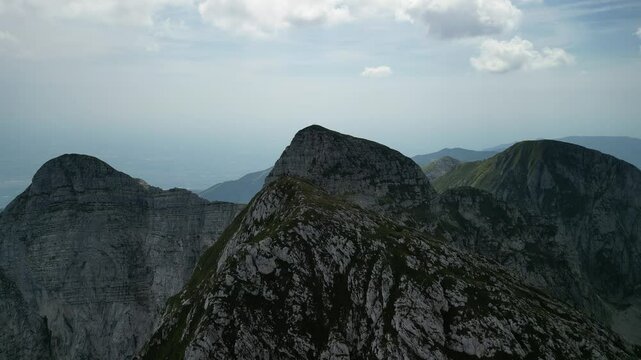 Drone flying over rocky mountains under a cloudy bright sky in summer in Levico Terme, Italy