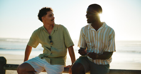 Men, talking and friends at beach for break with bonding, communication and support outdoor. Conversation, people and happy on fence, travel or summer vacation to relax with connection in nature