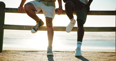 Men, legs and friends at beach for break with bonding, fashion shoes and support outdoor. Style, people and together on wood fence, travel or vacation to relax with connection in nature at sunset