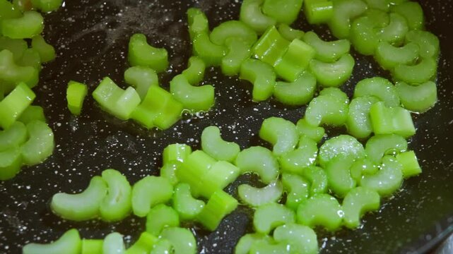 Food preparation. Close-up of sliced celery stalks in a frying pan, in hot olive oil. Slow motion footage 100fps.