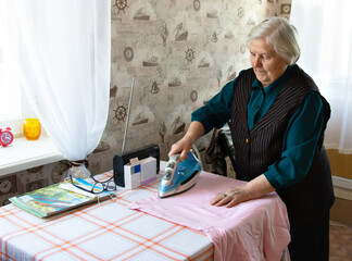 Portrait of an elderly 80 year old woman holding an iron and ironing on an ironing board