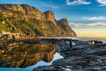 A solo surfer prepares to enter the water - set against a beautiful mountain backdrop at dawn. The tranquil scene embodies communion with nature
