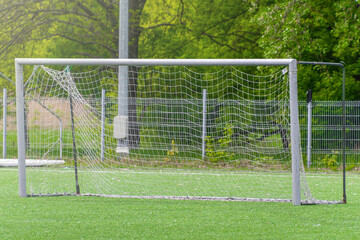 Empty soccer goal on green field with metal fence and trees in background