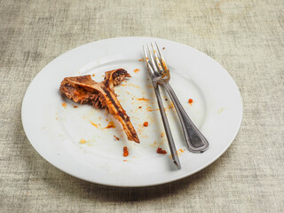 Finished high quality meal. Empty dirty plate with t bone, fork, knife. Fine dinner concept. Scraps on a plate.