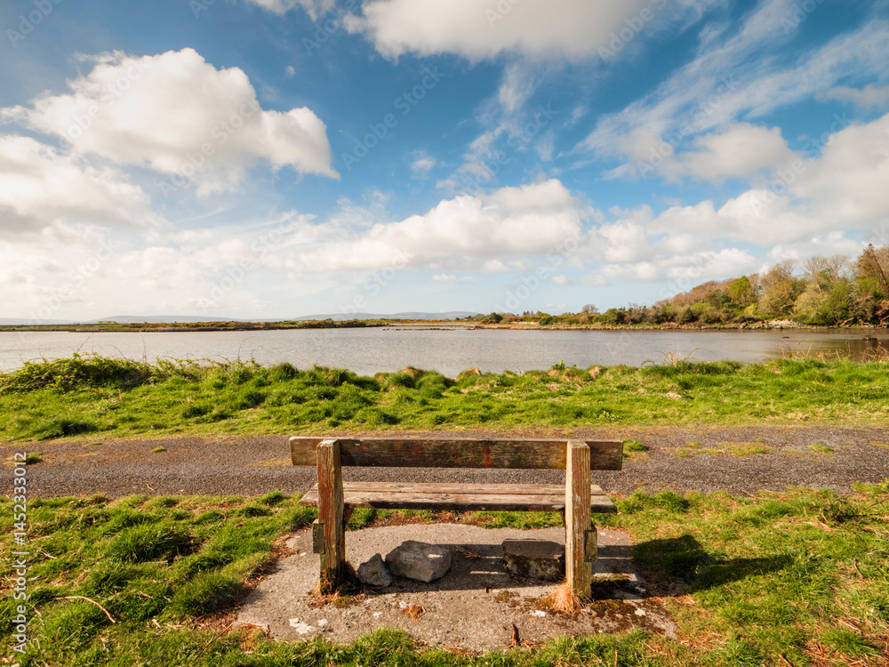 Fototapete one wooden old bench by a walking path with stunning view on open space with lake and amazing blue c
