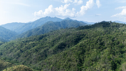Naklejka premium Lush green mountains covered with dense forest under a partly cloudy sky.