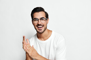 Smiling man with glasses wearing white t-shirt clapping hands in excitement, showcasing joy and...