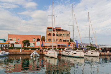 Portorosa port in Tonnarella city in Sicily. Sailing travel vacation. Sailing yachts and dinghy boats on the sea water surface under the blue sky. Marina with rosy buildings in Sicily, Aeolian Islands © Create.Pictures