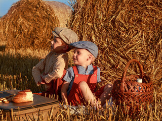 Two boys, brother, friend, child vintage dressed sitting near bale of straw and going to eat loaf of bread with milk, harvesting, cap, copyspace, texture, summer, emotions