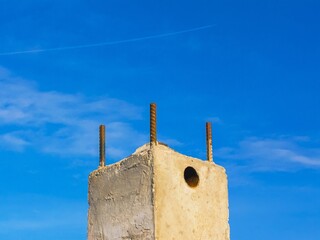 Concrete pillar with rebar protruding upwards against a vast, cloudless blue sky in daytime.