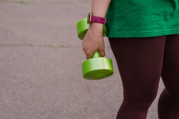 A woman in a green t-shirt performs a dumbbell shoulder press exercise during an outdoor workout...