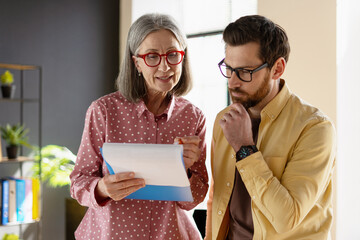 Senior businesswoman showing document to thoughtful businessman in office
