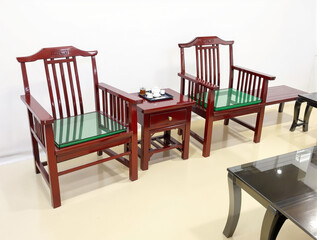 two elegant dark red wooden chairs with green glass cushions and a matching side table