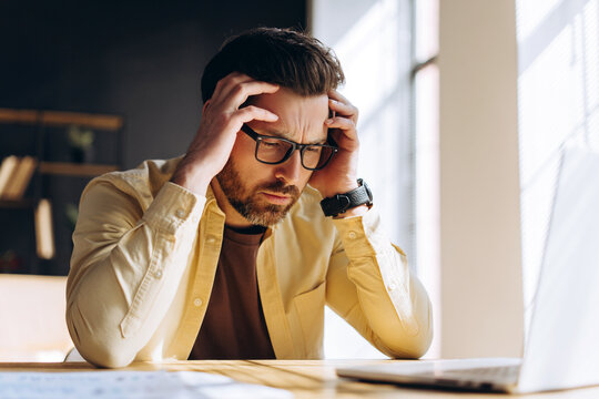Stressed businessman having headache while working on laptop - Powered by Adobe