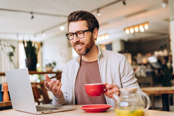 Happy businessman having a video call in a cafe while drinking tea