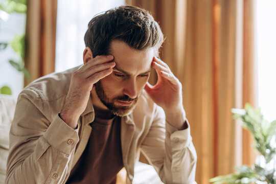 Stressed man suffering from headache touching temples at home