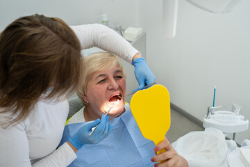 female dentist with elderly woman looking together to the mirror in the dental office. Healthy...