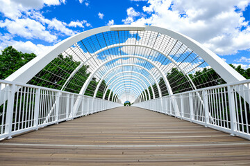 modern white pedestrian bridge with wooden deck under blue sky