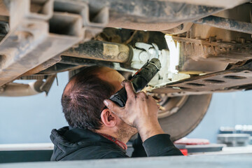 Mechanic inspecting car chassis with flashlight in repair shop