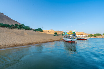Tourist boats dock at a sandy port in a Nubian village. Sandy hills and power lines in the...