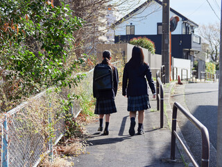 春の朝の住宅地に登校中の姉妹学生の後ろ姿