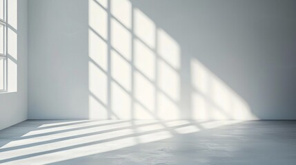 Fototapeta premium Sunlight filters through large windows, casting intricate shadow patterns on the bare concrete floor of a minimally decorated room. The atmosphere feels calm and spacious