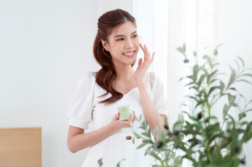 Fototapeta premium Woman Enjoying Natural Skincare in a Bright, Minimalistic Room Surrounded by Greenery