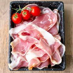 thinly sliced cured ham with cherry tomatoes in a black dish