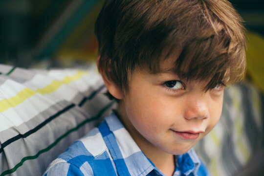 Close-up portrait of a smiling boy with brown hair sitting next to his bed