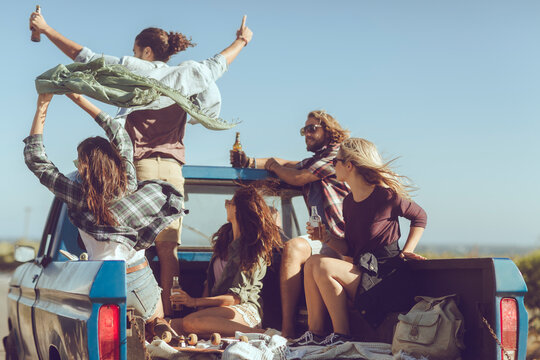 Young and diverse group of people riding in the back of an oldtimer truck on a sandy beach road while on a road trip