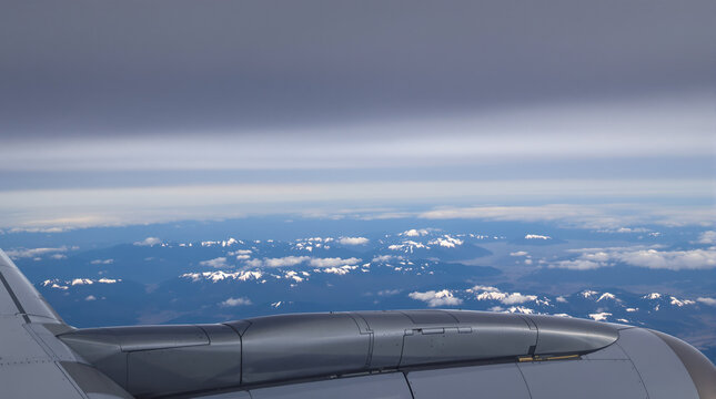 airplane view of snow-capped mountains from above the clouds