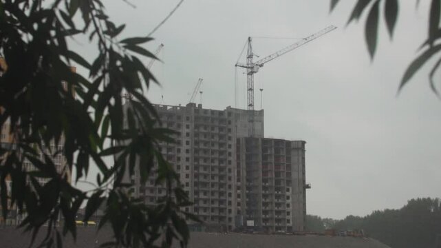 House under construction, construction crane, view through tree foliage.
