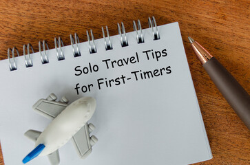 Solo Travel Tips for First Timers text on white notepad with toy airplane and pen