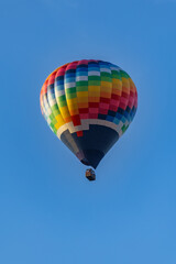 Colorful hot air balloon flying in a clear blue sky above red-tiled rooftops of residential buildings during golden hour