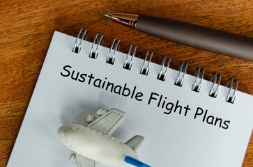 Sustainable Flight Plans text on white notepad with small airplane and pen background....